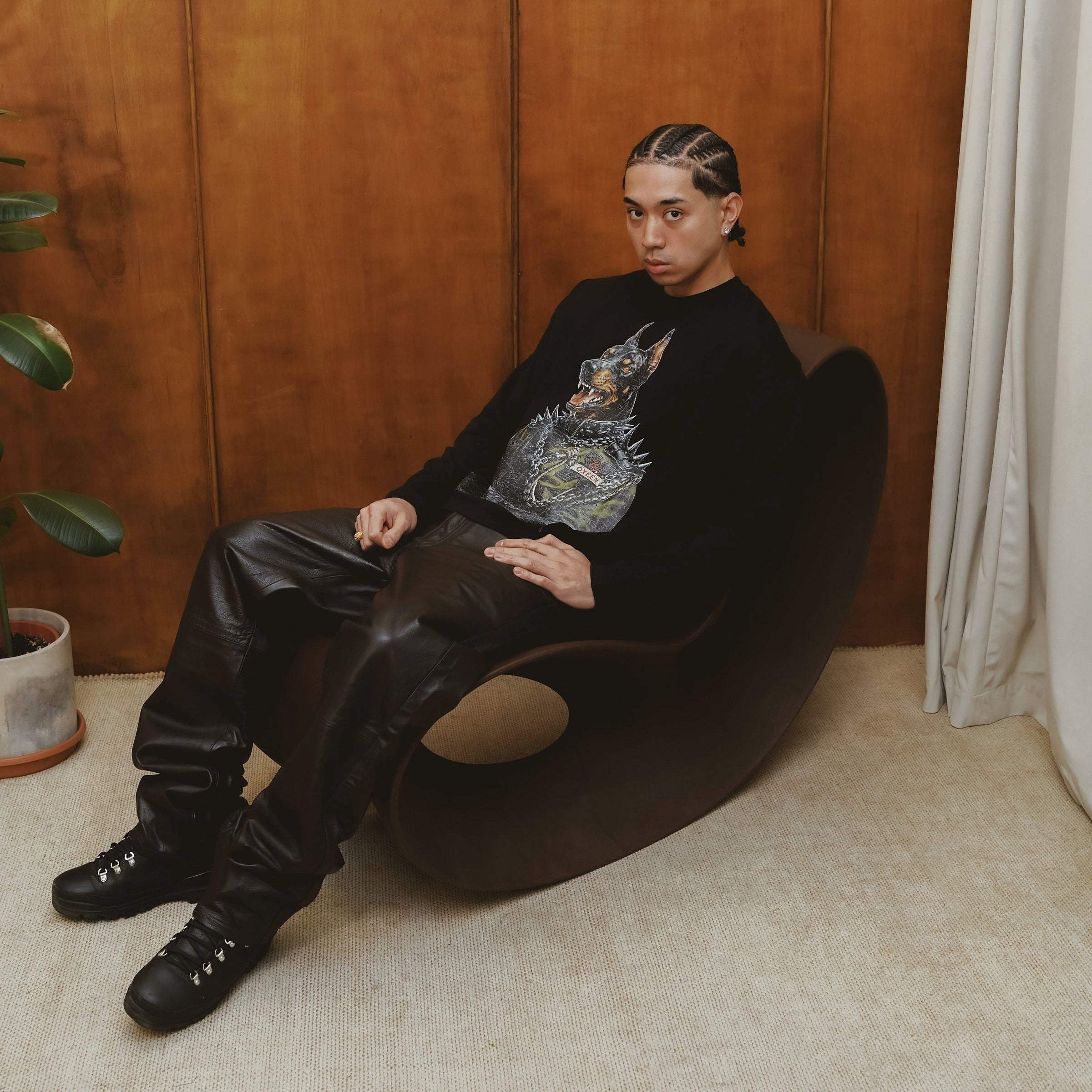 Person sitting on a black chair against a wooden paneled wall.